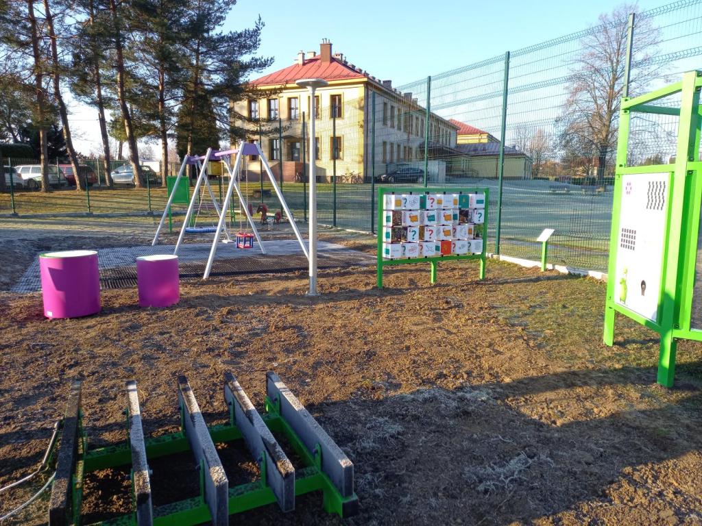 plac zabaw - urządzenia, ogrodzenie, w tle budynek szkoły