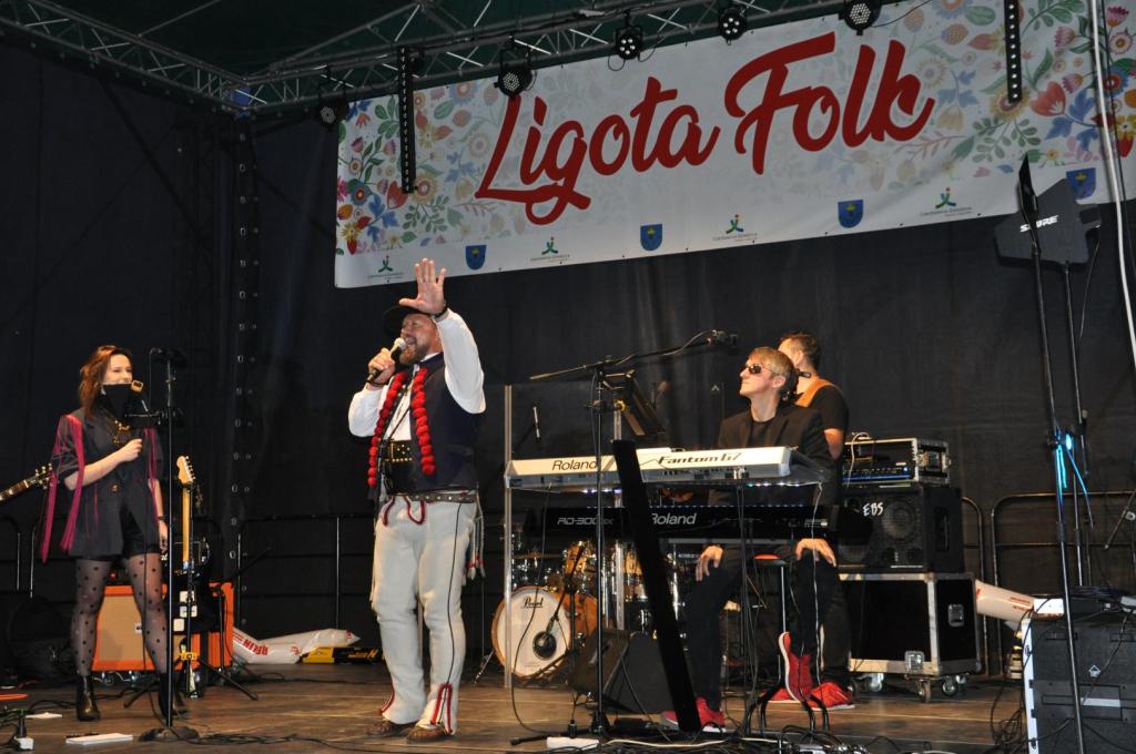 na scenie baner z napisem ligota folk, stoi konferansjer w stroju góralskim, w tle muzycy zespołu kryptonim