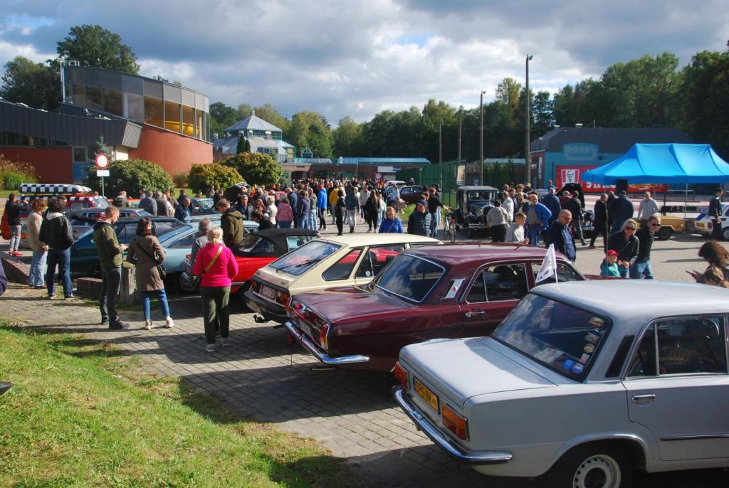 Widok na parking przed pływalnią, gdzie są zaparkowane pojazdy zabytkowe