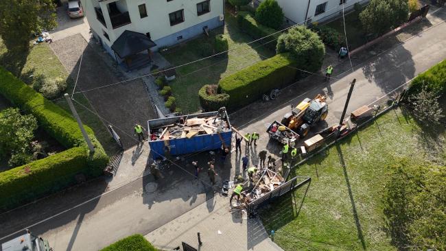 kontener na śmieci i pracujący przy sprzątaniu wolontariusze i żołnierze