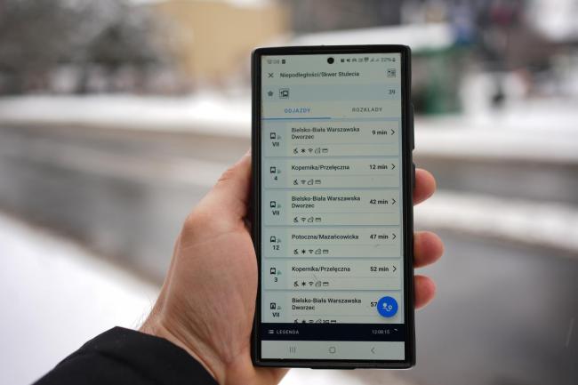 telefon z aplikacją na tle przystanku autobusowego